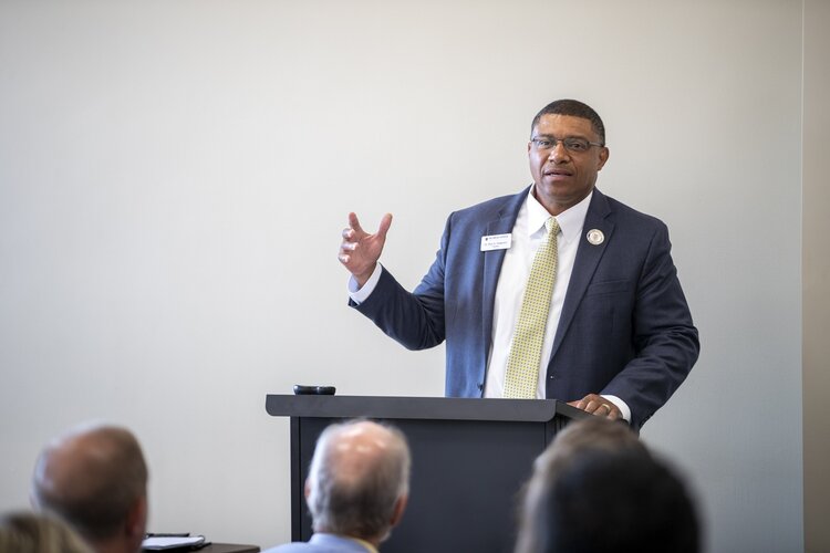 Dr. Ron K. Patterson in a navy suit speaking in front of a group of people.