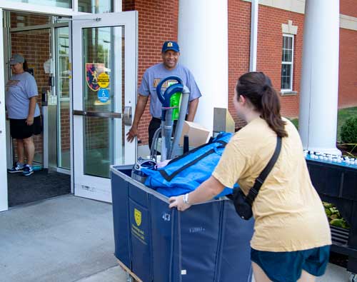 Dr. Patterson holds the door open for a student pushing a cart as she moves in to the Residence Hall